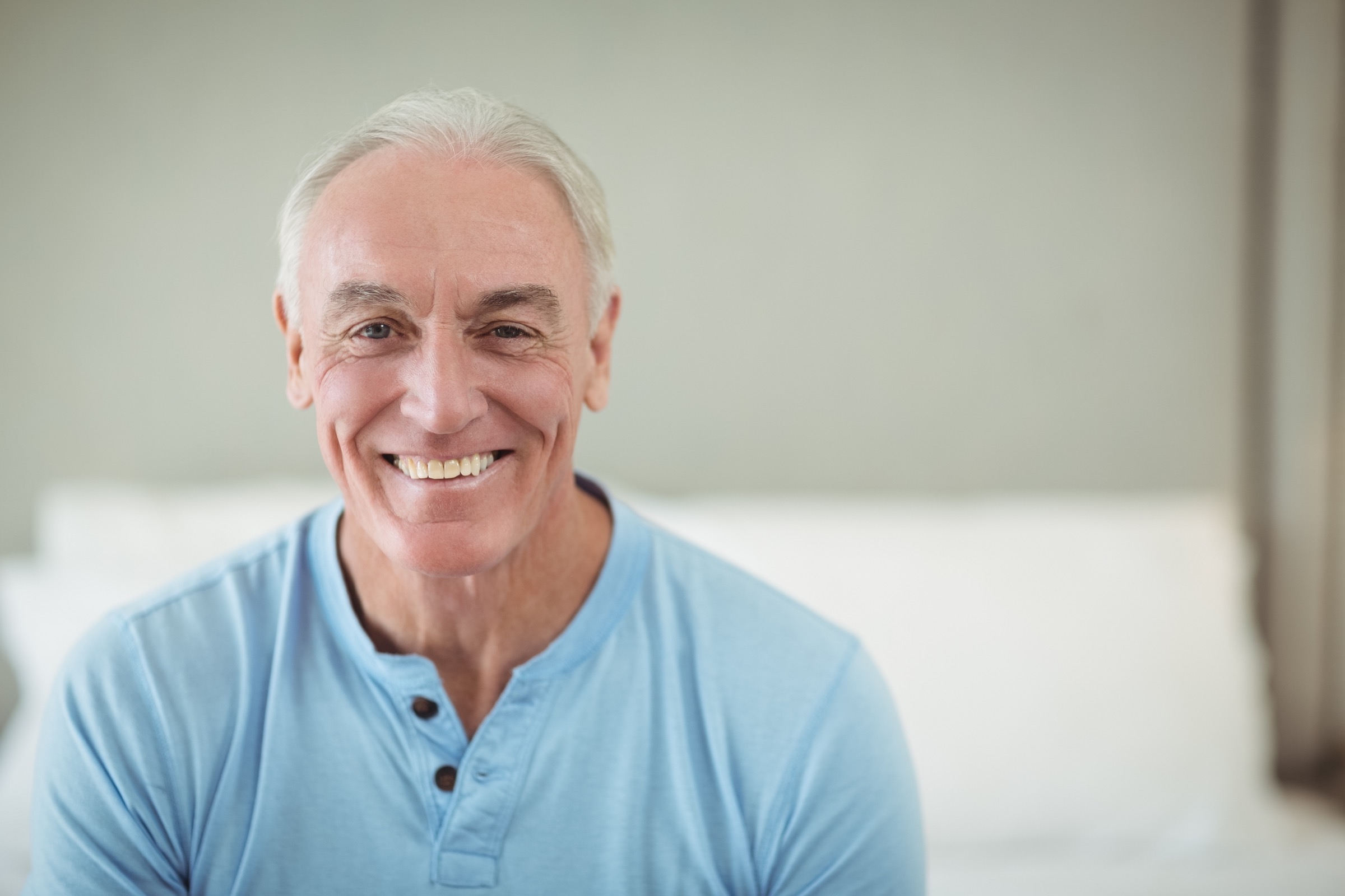 An older man smiling while sat on his bed