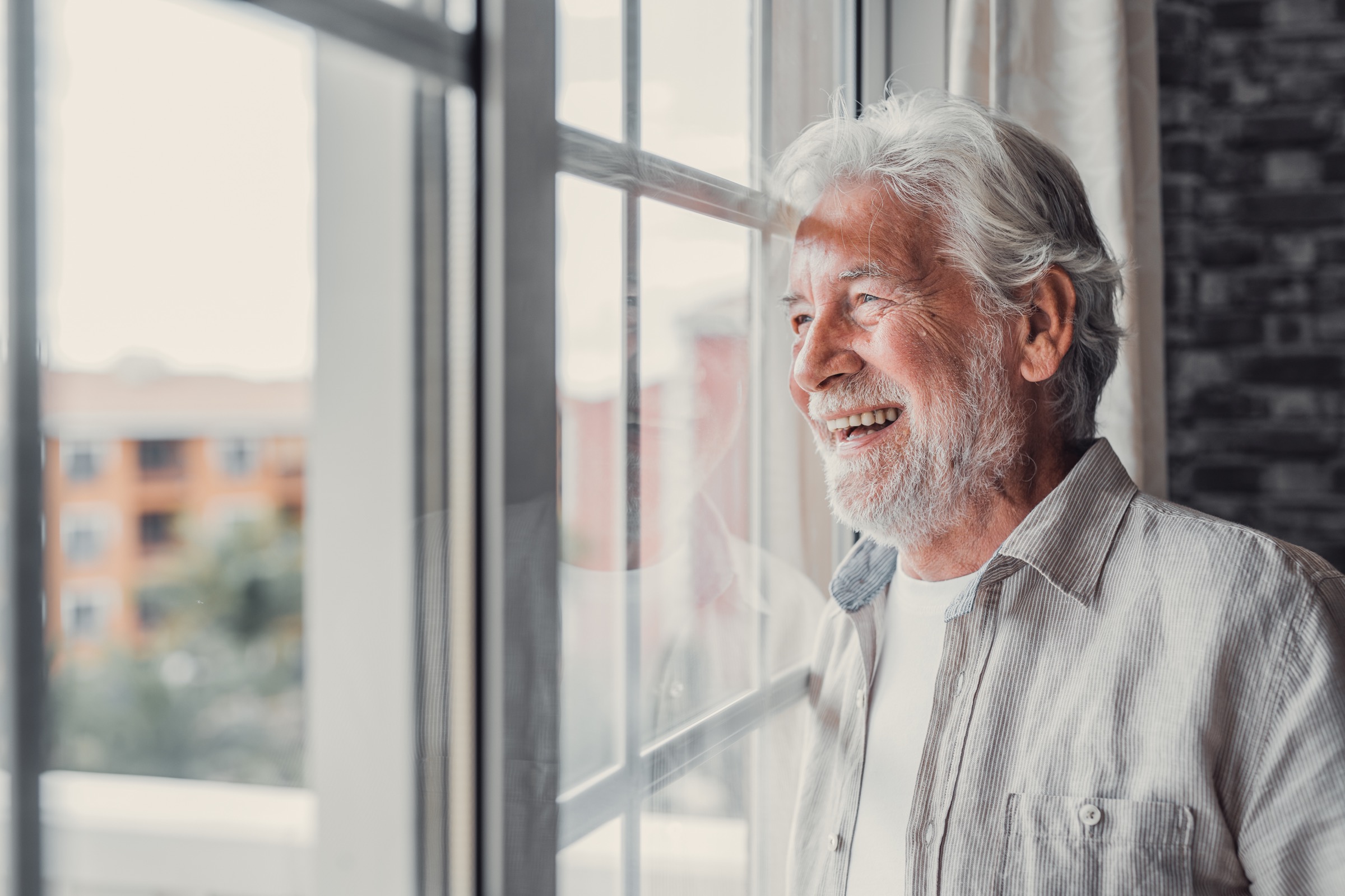 Older man smiling while looking out his window